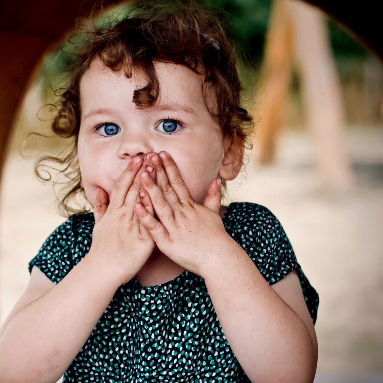 young child with both hands over mouth oops